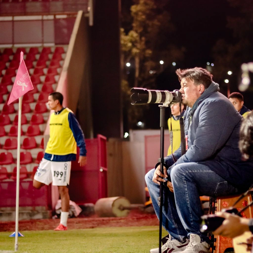 A college football head coach paces the sideline under stadium lights during a night game.
